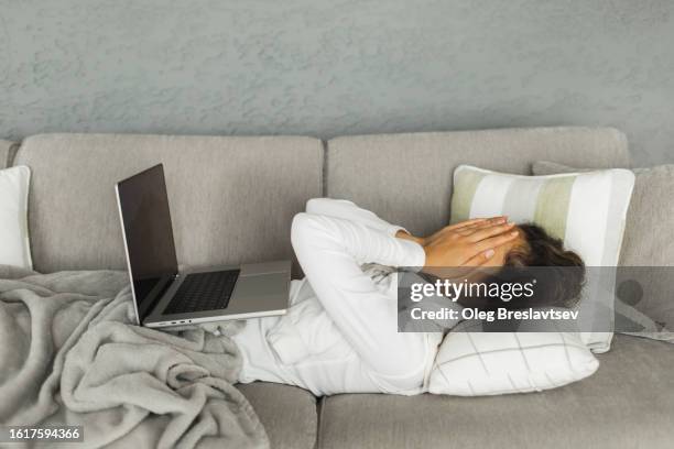 woman lying down on sofa and crying with face closed by hands after sad movie on laptop - midlife crisis stock pictures, royalty-free photos & images