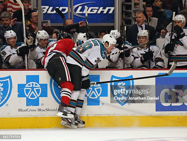 Logan Couture of the San Jose Sharks knocks Duncan Keith of the Chicago Blackhawks over the boards in front of the Shark bench at the United Center...