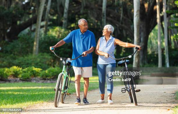 pareja afroamericana mayor caminando con bicicletas - gente de tercera edad activa fotografías e imágenes de stock