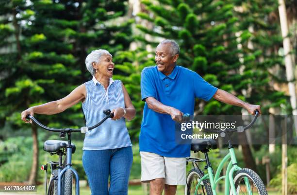 senior african american couple walk with bikes, laughing - black shorts stock pictures, royalty-free photos & images