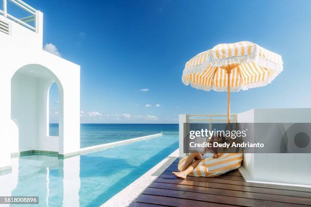beautiful indonesian relaxing under yellow stripped umbrella at the infinity pool side - empreendimento turístico imagens e fotografias de stock