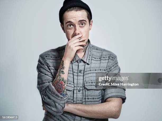 man with shirt and hat covering face with hand. - mano tapando la boca fotografías e imágenes de stock