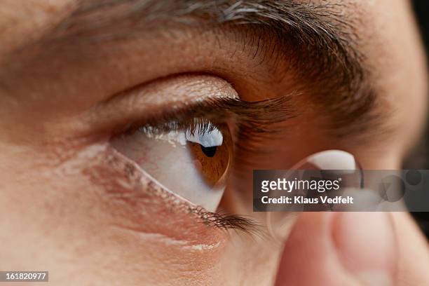 close-up of man putting in contact lens - lente a contatto foto e immagini stock