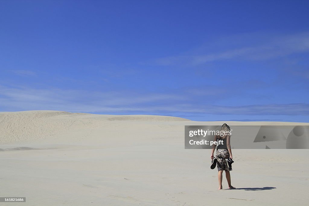 Lonely girl walking in sand dunes / desert