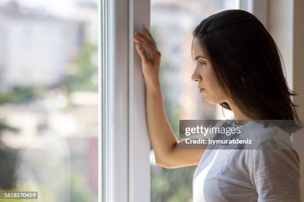 lonely woman looking out window - eating disorder stock pictures, royalty-free photos & images