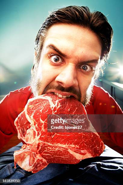 a man holding a large raw piece of meat with his teeth - red meat stock pictures, royalty-free photos & images