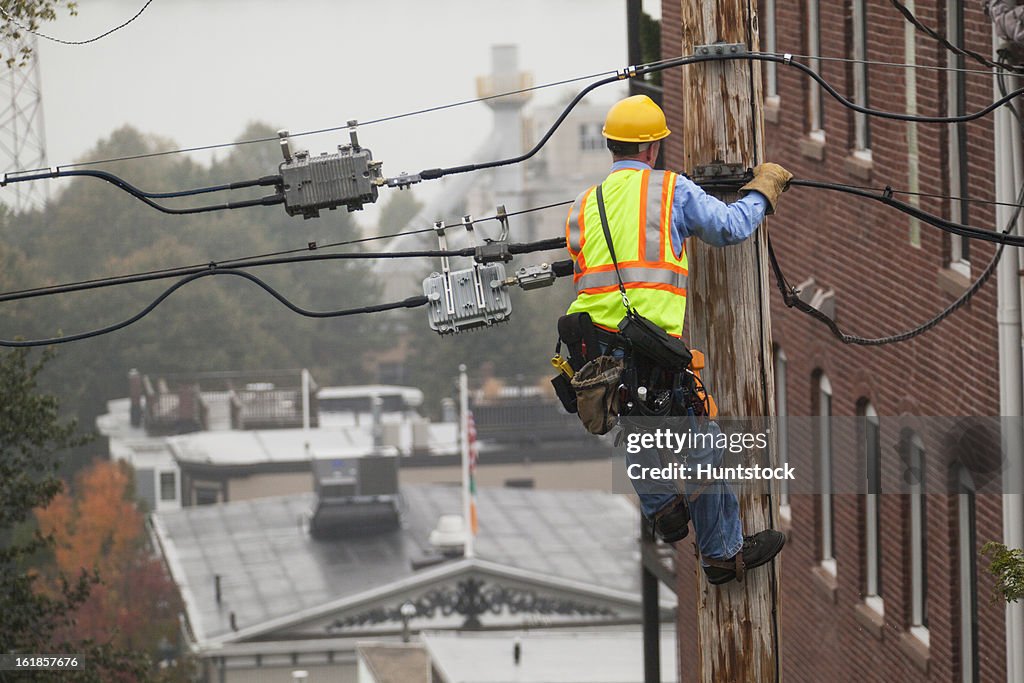 Cable lineman using lineman spikes to climb down pole