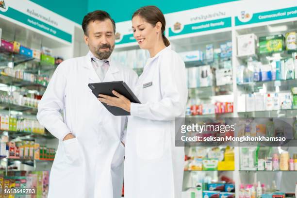 two pharmacists talking while examining a list of medical supplies. - female pharmacist with a digital tablet stock-fotos und bilder