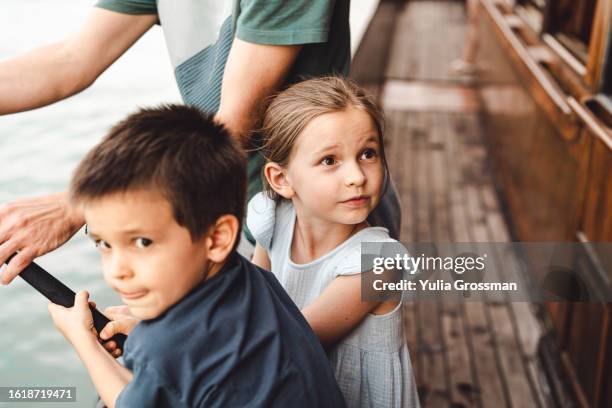 dad teaches his children (a girl and a boy) to fish. in the frame, men's hands hold a fishing rod and help children cope with the fishing line. the girl looks away in surprise. it seems that someone has caught a fish nearby! - family picture frame stockfoto's en -beelden