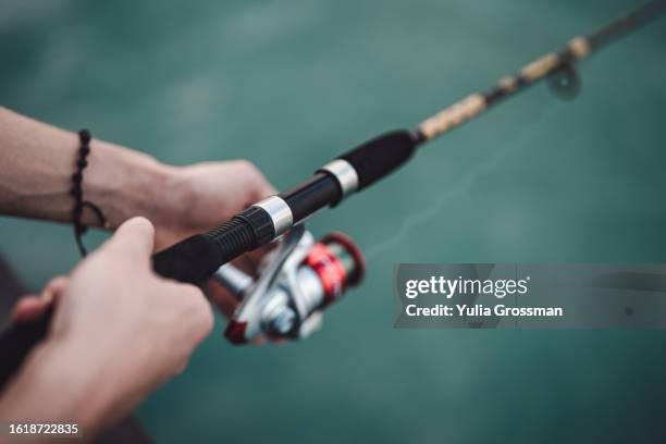 men's hands hold a fishing rod against the background of the turquoise sea. - profesional amateur stock pictures, royalty-free photos & images