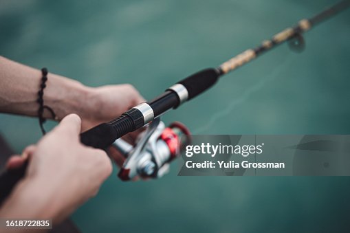 Men's hands hold a fishing rod against the background of the turquoise sea. Men's hands hold a fishing rod against the background of the turquoise sea.