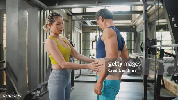a beautiful asian mid-adult woman fitness instructor using an orthopedic corset for back support for an asian senior athlete man before starting circuit training , preventing backache and injury - orthopedic corset stock pictures, royalty-free photos & images