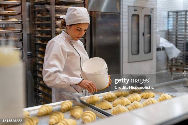 panettiere felice che diffonde la noce di cocco su alcuni croissant - panetteria foto e immagini stock