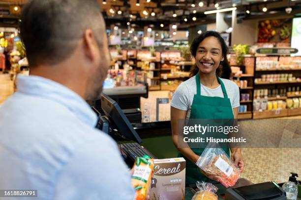 glückliche kassiererin, die im supermarkt arbeitet und die lebensmittel eines kunden registriert - markt verkaufsstätte stock-fotos und bilder