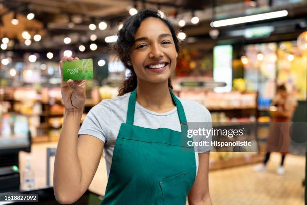 einzelhandelskauffrau, die in einem supermarkt arbeitet und eine kundenkarte in der hand hält - bonuskarte stock-fotos und bilder