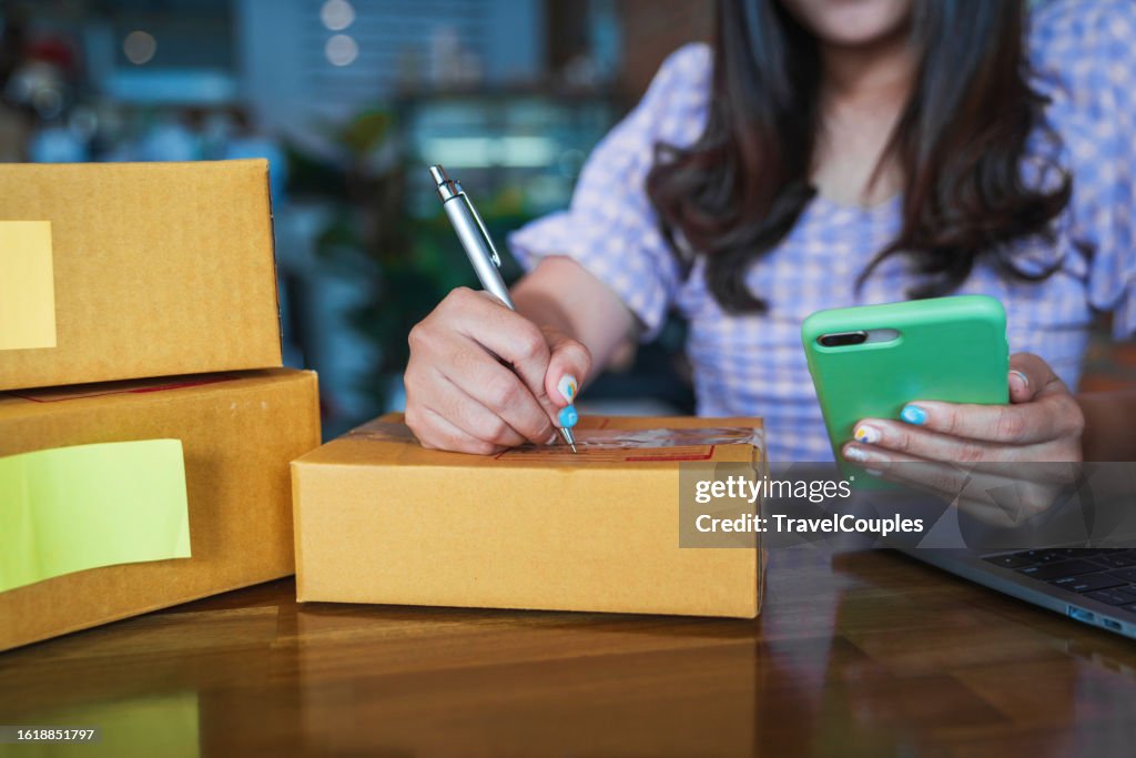 Young business woman working selling online. Entrepreneur owner using Laptop or tablet taking receive and checking online purchase shopping order to preparing pack product box. Online shopping