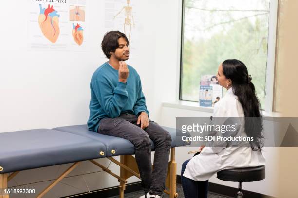 male adult patient gestures while explaining to the orthopedist where his pain is - american sign language stock pictures, royalty-free photos & images