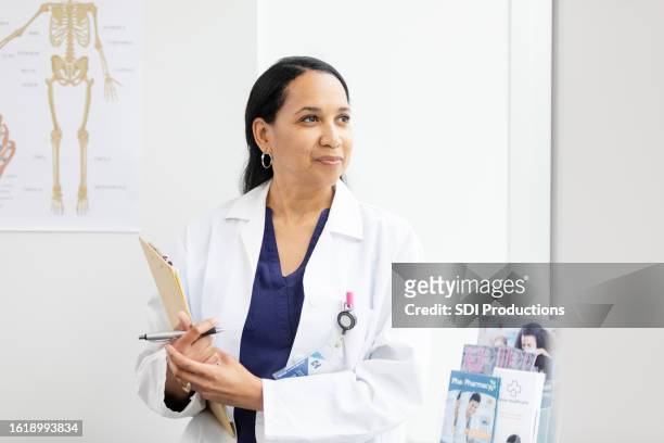 female doctor gazes out the window for a moment in between her medical appointments - orthopedist stock pictures, royalty-free photos & images