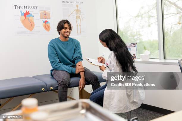 young adult male patient smiles while hearing the great news from the doctor - cuidados de saúde primários imagens e fotografias de stock