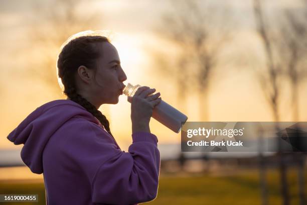 young female athlete is drinking smoothy after exercise at sunset. - sports drink stock pictures, royalty-free photos & images