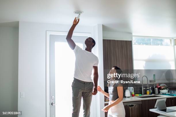 interracial couple installing smart energy efficient lightbulb - lampje-vervangen stockfoto's en -beelden
