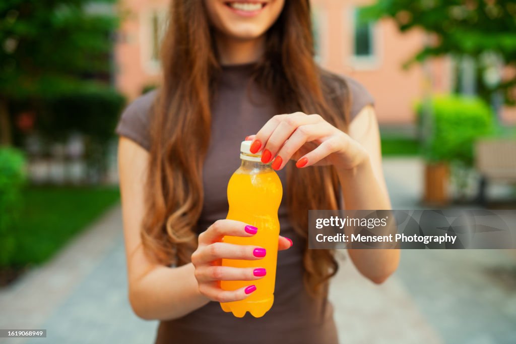 Close-up of an unrecognizable woman opening an orange bottle of lemon juice standing in city street background