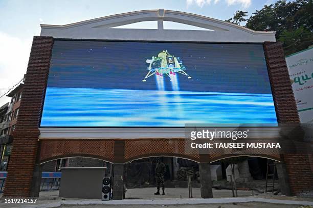 An Indian paramilitary trooper stands guard as a live telecast is aired near a clock tower in Srinagar on August 23 showing the Chandrayaan-3...