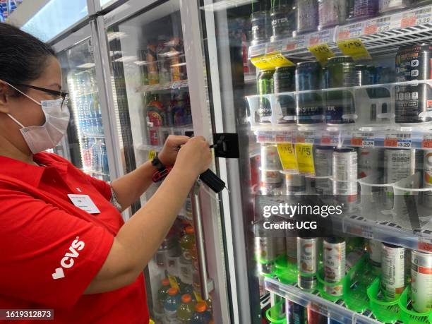 Pharmacy employee unlocking refrigerator to access energy drink for customer, Queens, New York.