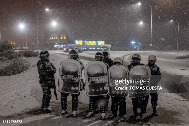 Police officers guard a Diarco supermarket under falling snow after an attempted looting, in Bariloche, Rio Negro Province, Argentina, on August 23,...