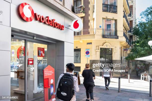 Pedestrians walk past a British multinational telecommunications corporation and phone operator, Vodafone, store in Spain.