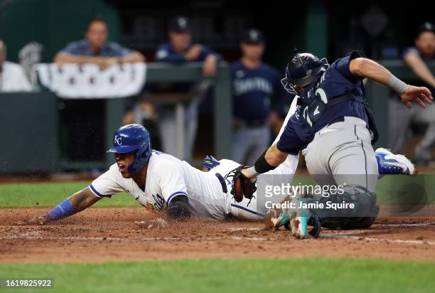 Salvador Perez of the Kansas City Royals slides headfirst into home plate to score as catcher Cal Raleigh of the Seattle Mariners is too late with...