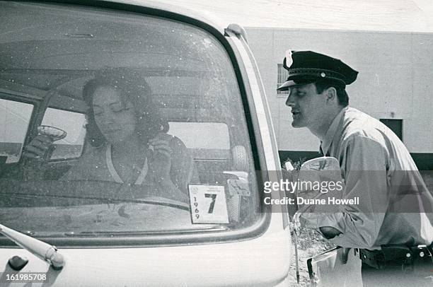 Policewoman Barbara Walley, playing part of a drunk driver, goes right on with her drinking in locked car as probationary Patrolman J. Thomas Myers...