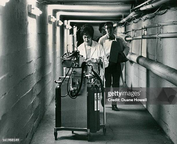 Miss Annabelle Tarman, nurse anesthetist, pushes an anesthesia gas machine down hall through tunnel from old Denver General Hospital to operating...