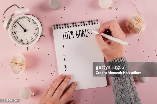 woman's hand writing goals 2024 for new year. new year routine. pink background with festive decoration. flat lay style - resolução de ano novo - fotografias e filmes do acervo