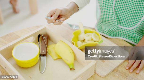 elementary mixed girl eating banana at table - qualifying school stock pictures, royalty-free photos & images