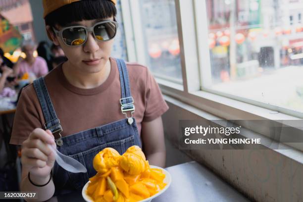 the young woman eats mango ice refreshingly during summer travel, which is quite refreshing and thirst-quenching. - mango shaved ice stock pictures, royalty-free photos & images