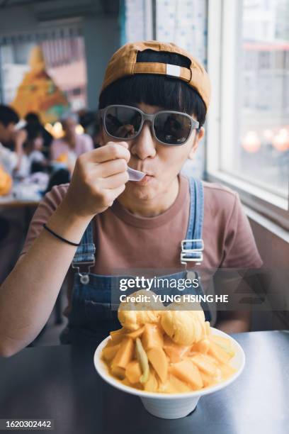 the young woman eats mango ice refreshingly during summer travel, which is quite refreshing and thirst-quenching. - mango shaved ice stock pictures, royalty-free photos & images
