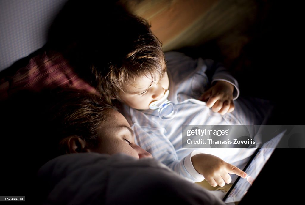 Small boy looking at a tablet while his mother sle