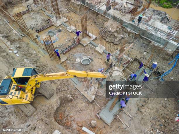 aerial view a construction site excavator is helping to lift steel for workers to assemble into the construction foundation. - waste wealth stock pictures, royalty-free photos & images