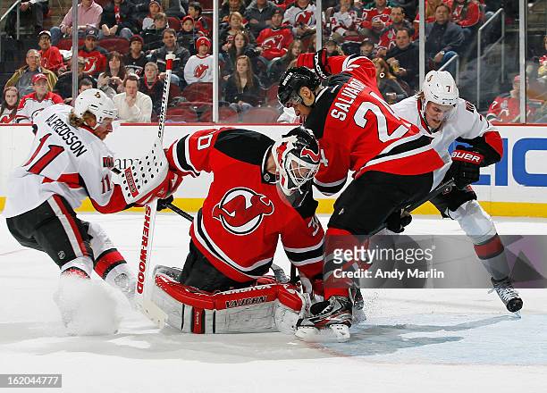 Martin Brodeur of the New Jersey Devils turns and makes a save as Bryce Salvador battles for the rebound in the crease against Daniel Alfredsson and...