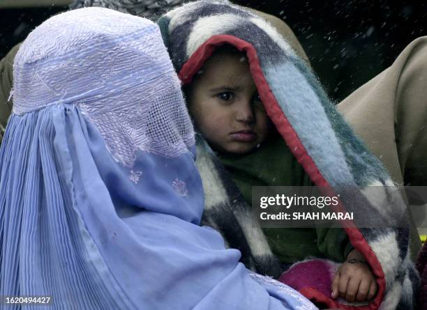 An Afghan woman holds a child as she waits in a snowstorm for clothing to be given to her during a humanitarian distribution scheme in a refugee camp...