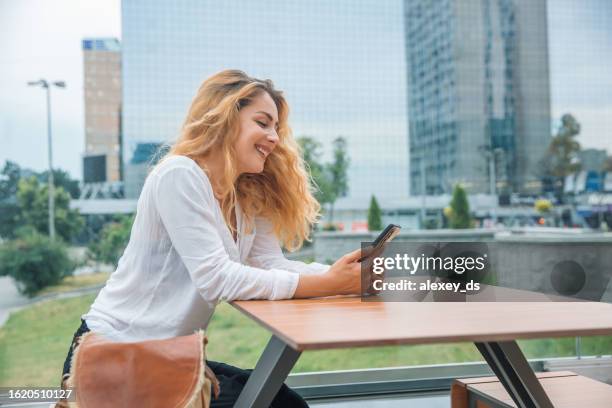 frau sitzt in einem restaurant und schaut mit einem lächeln auf das telefon - office smile light stock-fotos und bilder