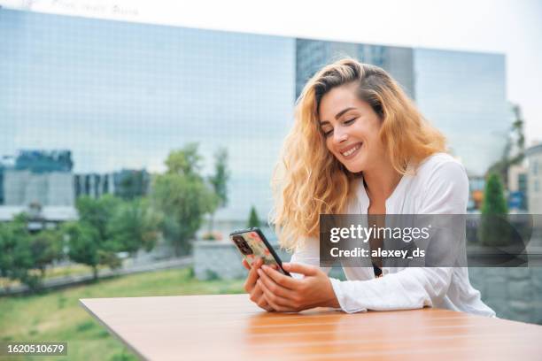 frau mit langen haaren sitzt in einem café und telefoniert mit einem lächeln - office smile light stock-fotos und bilder