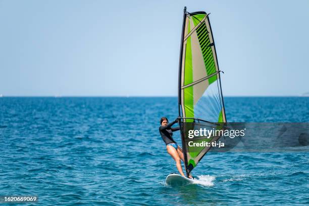 young girl windsurfing in a blue ocean - wind surfing stock pictures, royalty-free photos & images