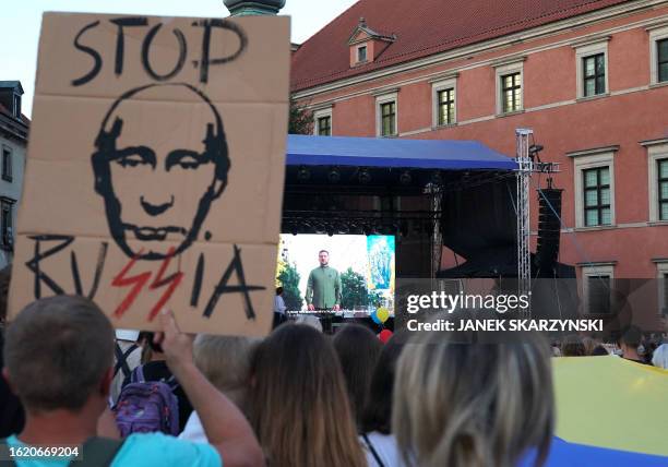 Ukrainian President Volodymyr Zelensky is seen on a screen as people gather to mark Ukraine's Independence Day while a demonstrator holds up a...