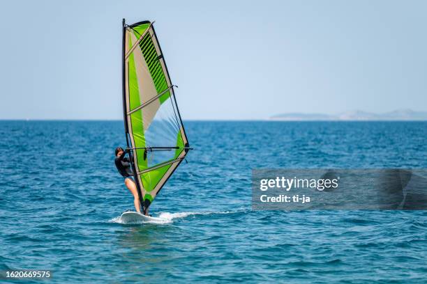 niña haciendo windsurf en un océano azul - windsurfing fotografías e imágenes de stock