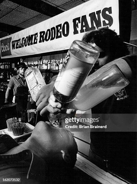 Texas steer roper Larry Noland leans back as bartender at Mayflower Bar mixes drink -»ver the bar-¡styte in his mouth.;