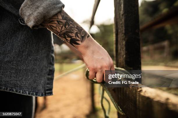 nahaufnahme von frauenhänden, die ein seil an einem zaun auf einer ranch binden - arm tattoos women stock-fotos und bilder