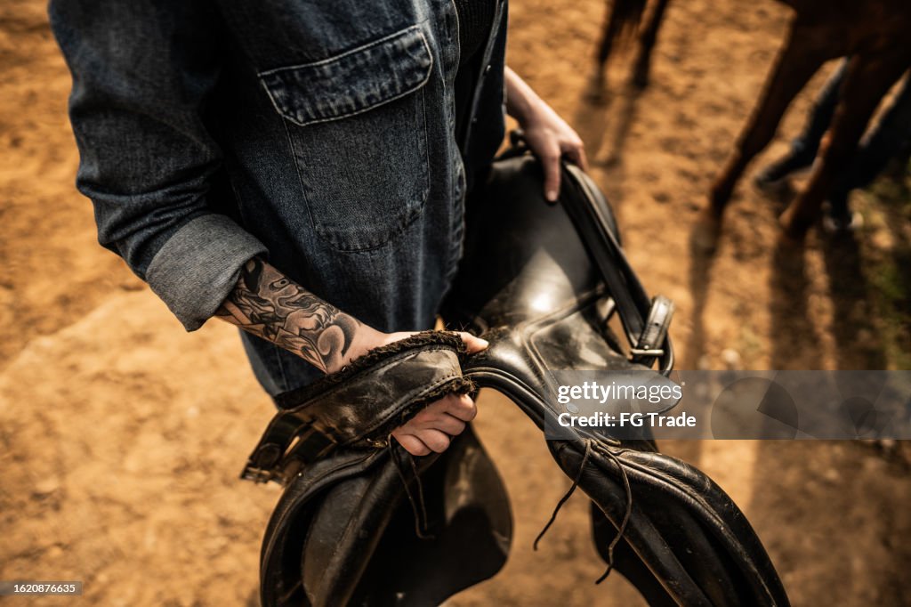 Nahaufnahme von Frauenhänden, die einen Sattel auf einer Ranch tragen