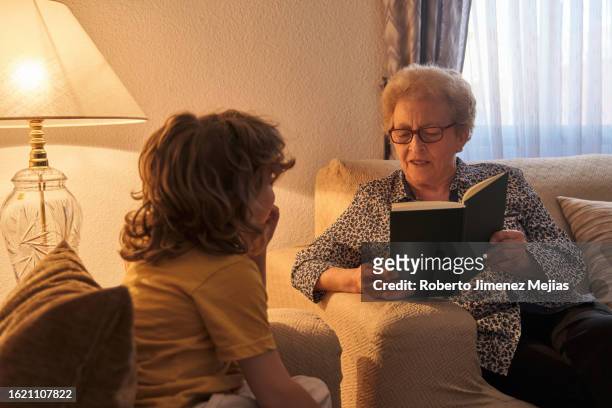 grandmother reading an adventure book to her grandson while he looks at her attentively. - literatur stock-fotos und bilder